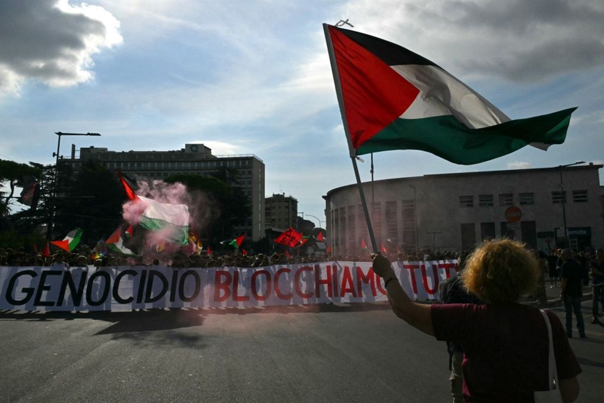 Orang-orang berbaris di belakang spanduk bertuliskan Melawan Genosida, Mari Kita Blokir Semuanya selama aksi mogok nasional sebagai bentuk solidaritas terhadap warga Palestina di Gaza dan menyerukan penghentian pengiriman senjata ke Israel, di Roma pada 22 September.